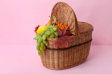 Pembe arka planda farklı taze meyvelerle dolu bir sepet.