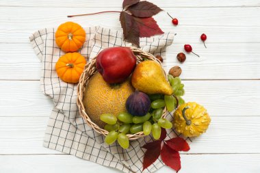 Beyaz ahşap arka planda farklı taze meyveler ve balkabaklarıyla hasır sepet.