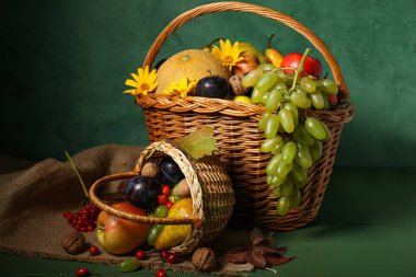 Yeşil duvarın yanındaki masada farklı taze meyvelerle dolu sepetler.