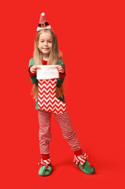 Kırmızı arka planda çorabı olan Noel cücesi kostümlü şirin bir kız.