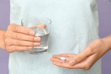 Leylak arka planında hapları ve bir bardak suyu olan kadın, yakın plan.