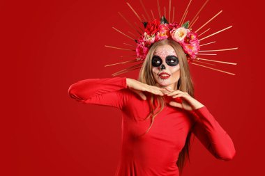 Kırmızı arka planda yüzü boyalı genç bir kadın. Meksika Ölüler Günü 'nün Kutlaması (El Dia de Muertos)