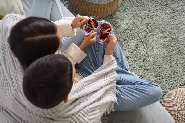 Couple with glasses of tasty mulled wine and warm blanket sitting on sofa in living room, top view