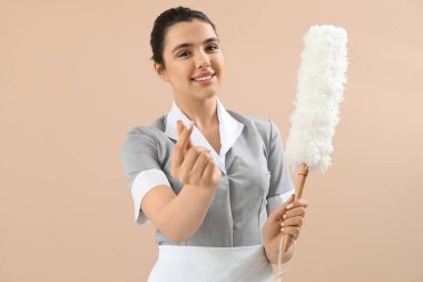 Güzel oda hizmetçisi bej arka planda parmaklarıyla kalp yapıyor.