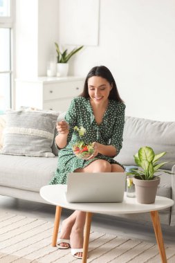 Evde elinde bir kase sebze salatası olan genç bir kadın sohbet ediyor.