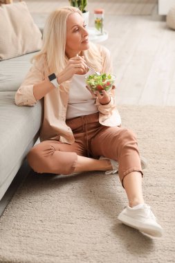 Evde sebze salatası yiyen olgun bir kadın.