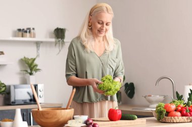 Olgun bir kadın mutfakta sebze salatası yapıyor.