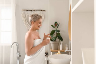 Olgun bir kadın banyoya yüz kremi sürüyor.