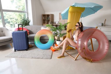 Yaz tatiline hazır genç bir kadın cep telefonuyla evde konuşuyor.