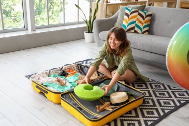 Evde bavuldan boyun yastığı çıkaran genç bir kadın var.