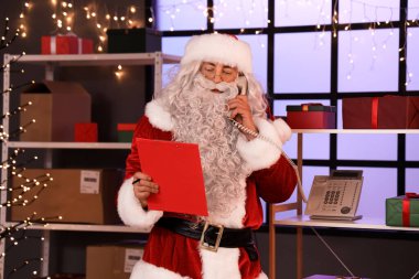 Elinde dosya olan Noel Baba postanede telefonla konuşuyor.