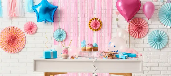 Tasty cupcakes with gifts for gender reveal party on table in room