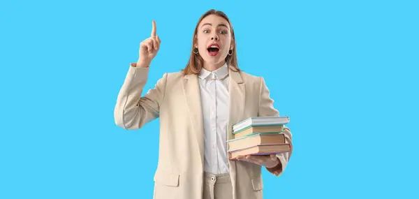 Young woman with books and raised index finger on light blue background