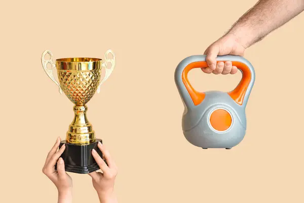 Female hands with gold cup and male hand with kettlebell on beige background