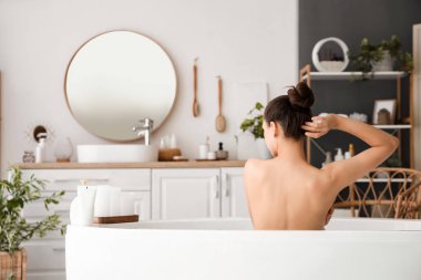 Genç bir kadın evde banyo yapıyor, arkadan bakıyor.
