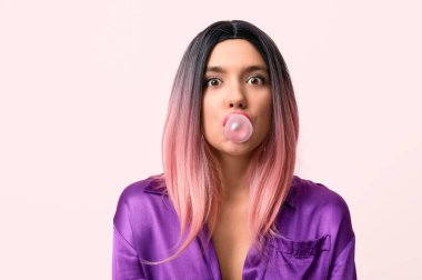 Pembe arka planda peruklu sakız çiğneyen güzel genç bir kadının portresi.