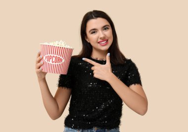 Güzel, genç, mutlu bir kadın bej arka plandaki patlamış mısırı işaret ediyor.