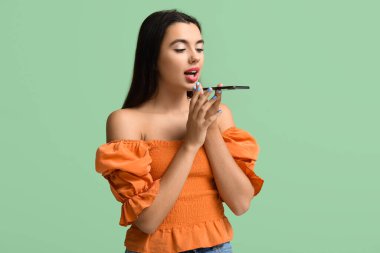 Güzel, mutlu, genç bir kadın yeşil arka planda cep telefonuyla konuşuyor.