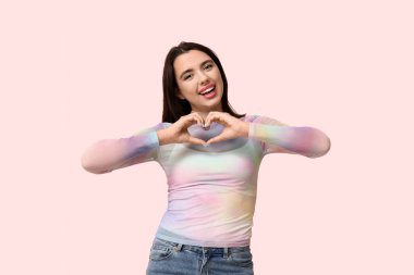 Güzel, genç, mutlu bir kadın pembe arka planda kalp hareketi gösteriyor.