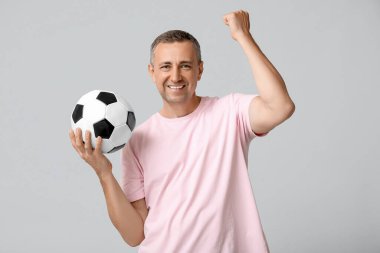 Gri arka planda futbol topu olan mutlu ve olgun bir adam.