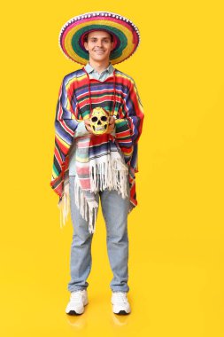 Sarı arka planda kafatasını boyamış sombrero giyen yakışıklı bir genç.