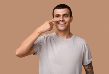 Genç adam kahverengi arka planda burnu işaret ediyor.
