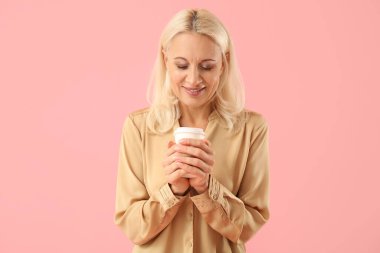 Pembe arka planda bir fincan kahveli olgun bir kadın.
