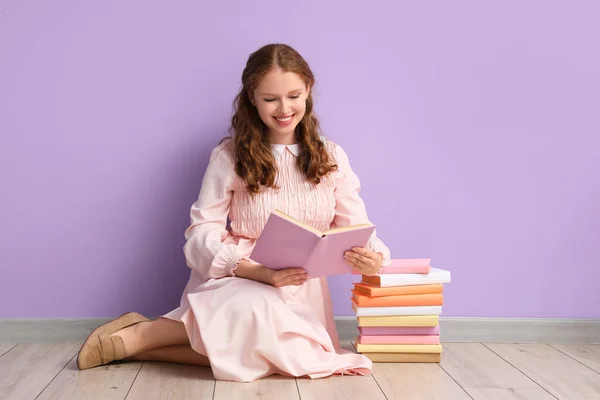 Young woman reading book near lilac wall