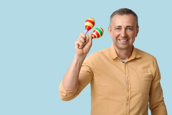 Handsome mature Mexican man with maracas on blue background