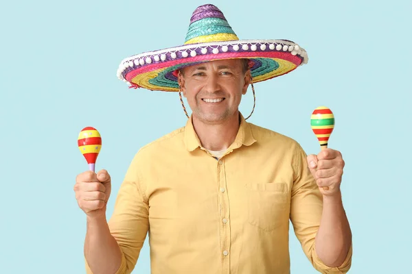 Handsome mature Mexican man in sombrero hat with maracas on blue background