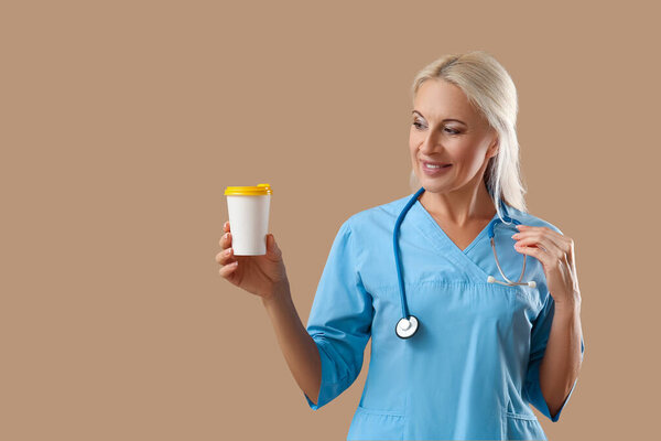 Зрелая женщина-врач с чашкой кофе на коричневом фоне