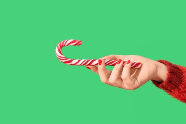 Kırmızı manikürlü kadın eli ve yeşil arka planda Noel şekeri bastonu.
