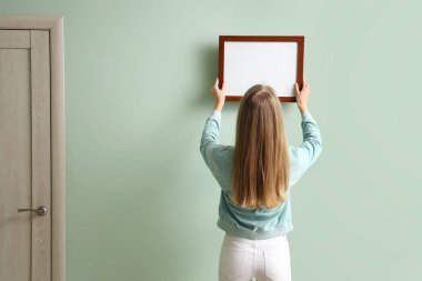 Evdeki yeşil duvara boş bir çerçeve asan genç bir kadın.