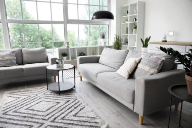 Işıl ışıl oturma odasının içi rahat gri koltuklar, kahve masası ve büyük pencereli.