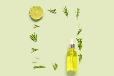 Bir şişe narenciye yağı, bitkiler ve soluk yeşil arka planda limon.