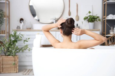 Genç bir kadın evde banyo yapıyor, arkadan bakıyor.
