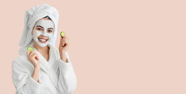 Beautiful young woman with cucumber slices and facial mask on pink background with space for text. Cosmetology concept