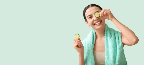 Beautiful young woman with cucumber slices on mint background with space for text. Cosmetology concept