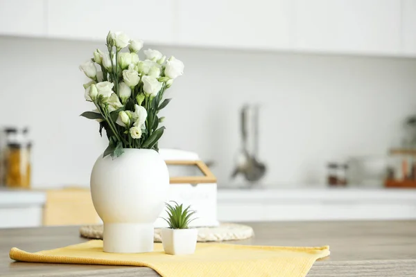 Vase with roses and succulent on table in light kitchen