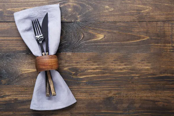 Modern silver cutlery with napkin on brown wooden background
