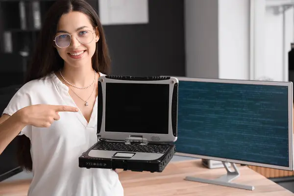 Pretty young female programmer pointing at blank screen of old laptop in office