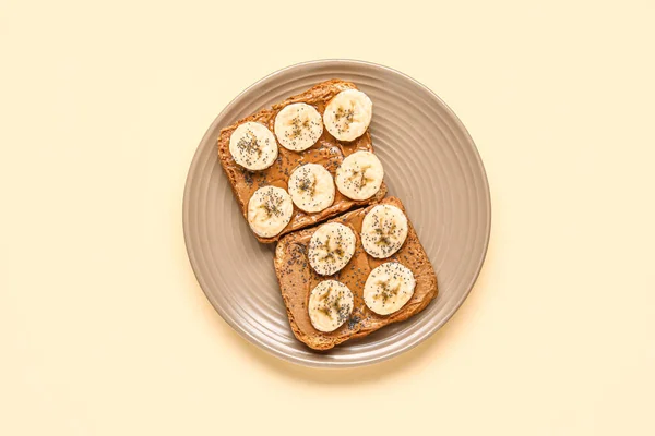 Plate of toasts with peanut butter, banana and poppy seeds on yellow background