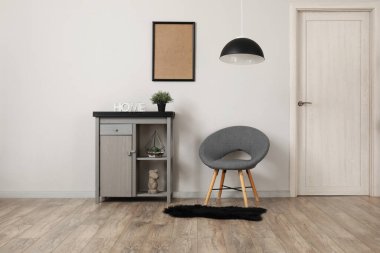 Beyaz duvarın yanında şık gri koltuğu ve modern dolabı olan oturma odasının içinde.