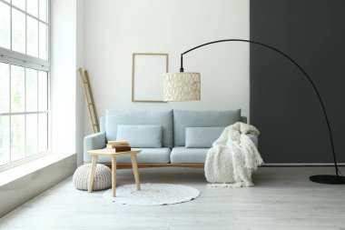 Işıl ışıl oturma odasının içi rahat gri kanepe ve taburede kitaplar.