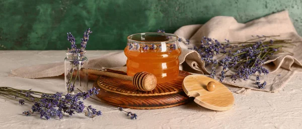 Jar of sweet lavender honey, dipper and flowers on white table