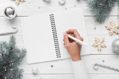 Not defterine Noel süsü ve beyaz ahşap arka planda kurabiyeler yazan kadın