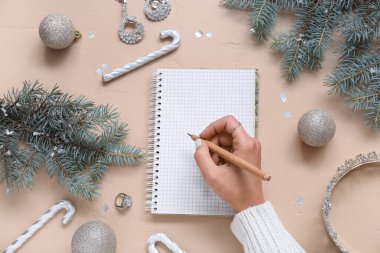 Not defterine Noel dekorasyonu ve bej arka planda aksesuarları olan bir kadın.