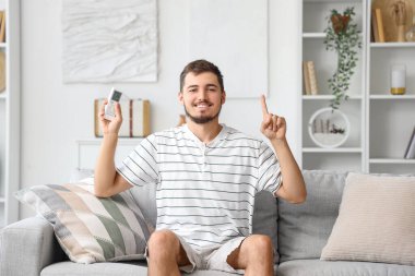 Klimalı genç adam, uzaktan kumandayla odadaki bir şeyi işaret ediyor.