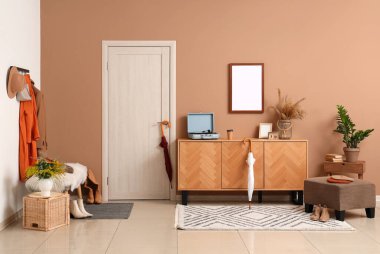 Modern koridorun içinde şık sonbahar kıyafetleri, sedir ve ahşap büfe var.