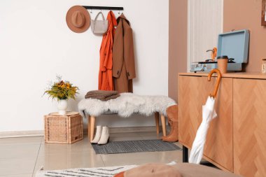 Modern koridorun içinde şık sonbahar kıyafetleri, bank ve ahşap büfe var.